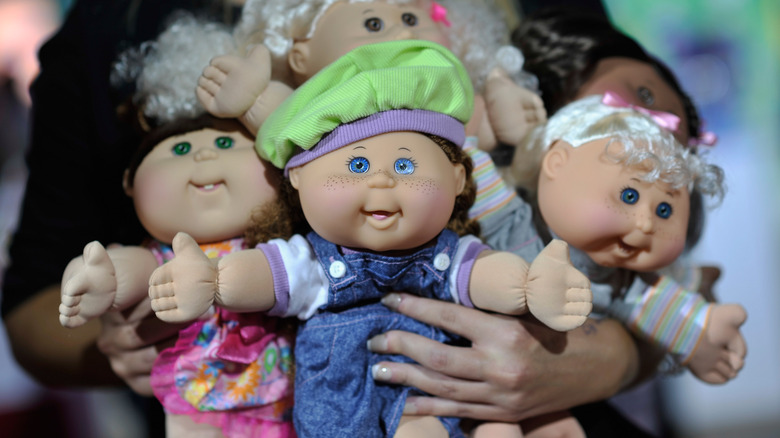 A woman holding several Cabbage Patch Kids dolls.
