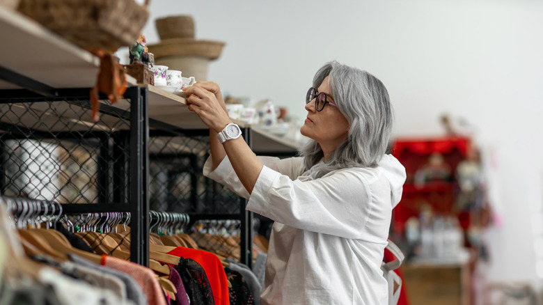 A woman reaching for teacups in a thrift store.