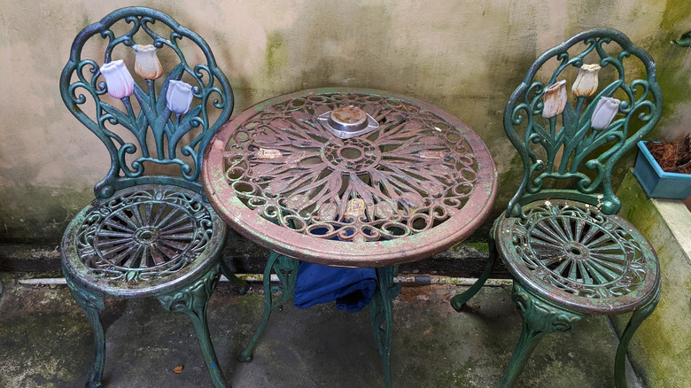 Two ornate floral chairs made of cast iron flank a matching cafe table