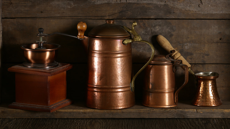 A vintage copper coffee cookware set sits on a wooden shelf