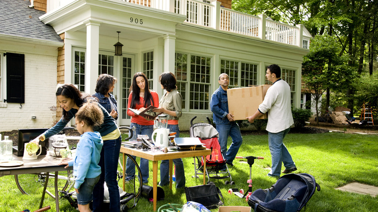 People look through items on tables at an estate sale in the front yard of a white house