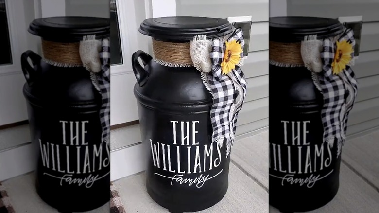A black antique milk pitcher that says "the williams family" and includes decorative ribbons and artificial sunflowers