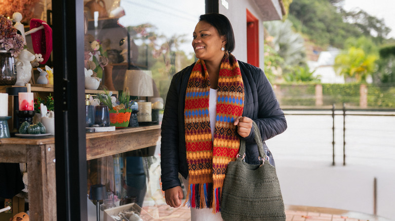 A woman smiles and looks into the window of a thrift store