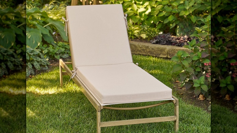 A cream colored cushion is tied to a neutral outdoor chaise lounge