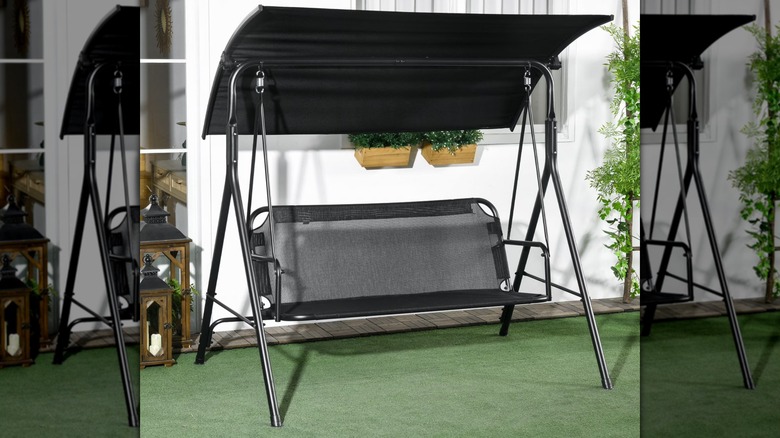 A black covered swing chair sits on a turf-covered patio