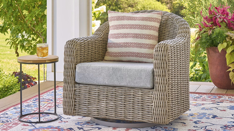A Better Homes & Gardens Bellamy Swivel Glider Patio Chair sits outside next to a small side table and potted plant