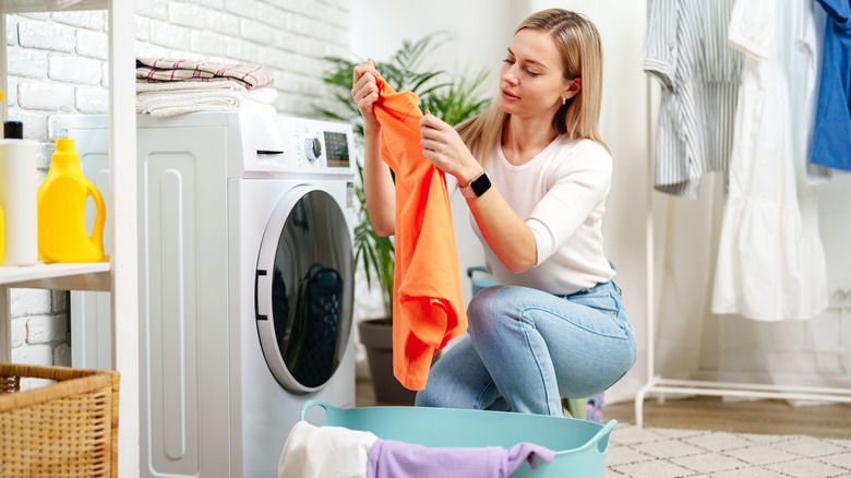 young woman examining colorful clothes next to a washing machine