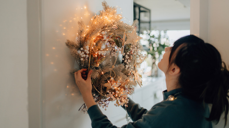 A person hangs up a lit wreath with white berries on it