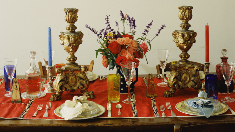 A table set with red runner, flowers, and candlesticks