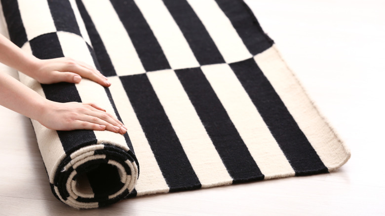 A pair of hands rolling a black-and-white carpet