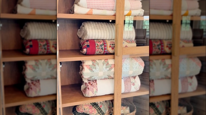 Colorful quilts folded behind glass panel of wooden china cabinet