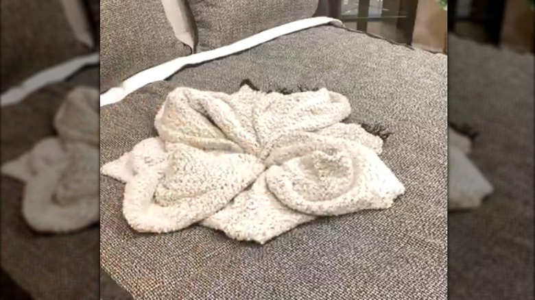 Soft blanket folded and tucked into a flower shape on gray bed