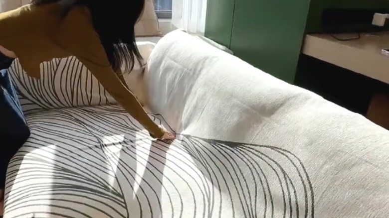 Woman tucking stylish blanket into couch cushions