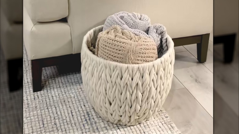 Thin crochet blankets rolled up in woven basket in neutral-colored living room