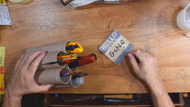 Cardboard tubes fashioned into multi-tiered holder for boxcutter, screwdriver, brushes, and writing utensils for garage workbench