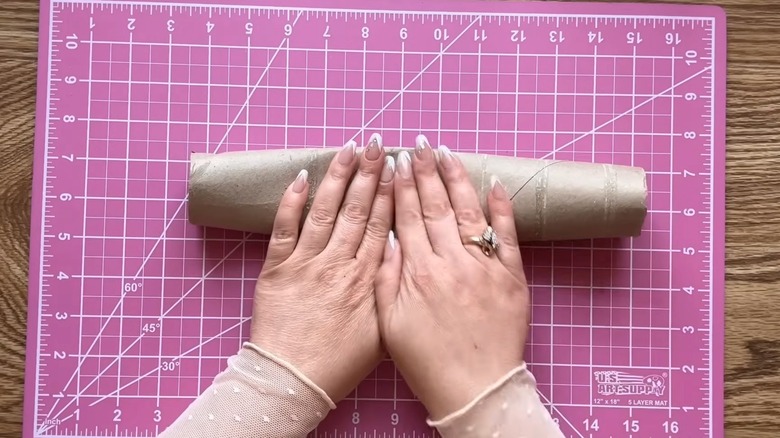Woman with manicured hands pressing down on paper towel roll for DIY project over pink cutting mat