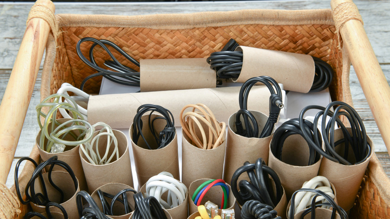 Assorted cords, cables, and wires in paper tubes in woven basket on wood deck