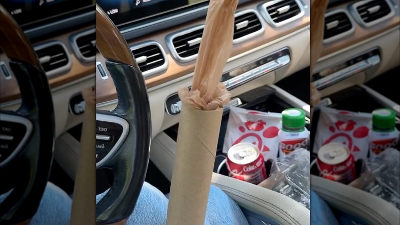 Woman pulling disposable plastic bags from cardboard tube in messy car