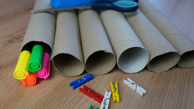 paper towel rolls on wood table with colorful highlighters and clothespins nearby