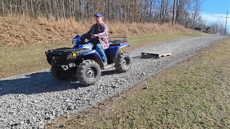 Man on an ATV dragging a pallet over a gravel driveway