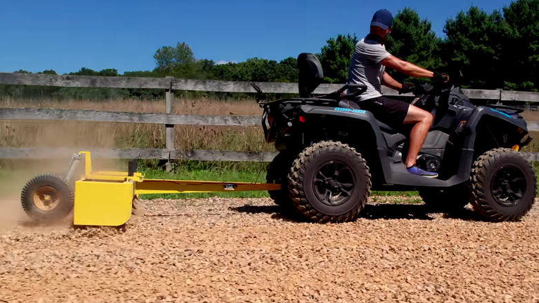 Man on ATV pulling a small box blade attachment over gravel