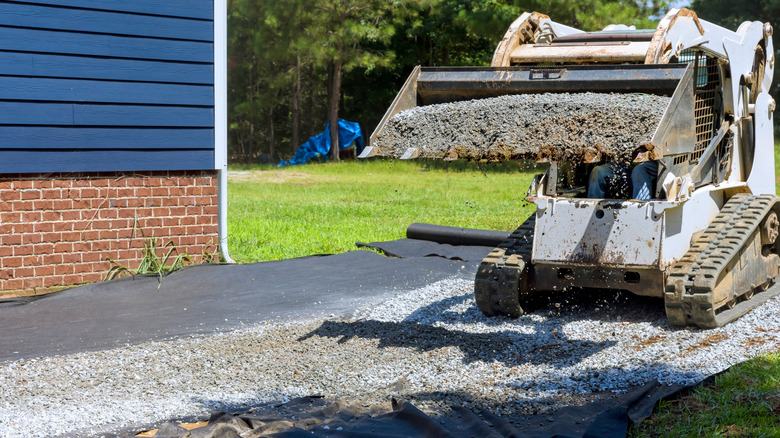 A tractorr spreading gravel on black tarp in home