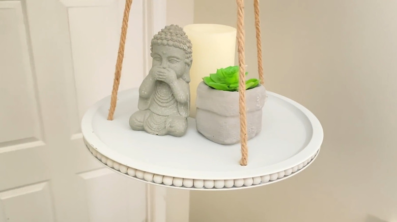 Hanging display shelf with rope hangers and decor pieces on it