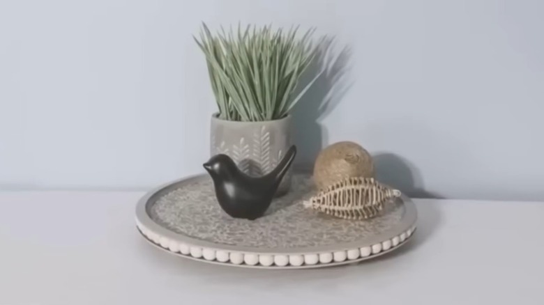 Two pizza pans with wood beads between and wood legs on the bottom with decor on top