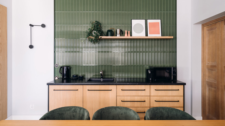 A small kitchen with a green backsplash and honey oak cabinets with black handles