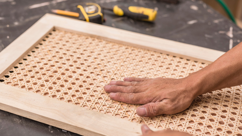 A man fastening cane webbing to a light wooden cabinet