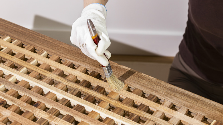 A gloved hand staining a wooden surface with a brush