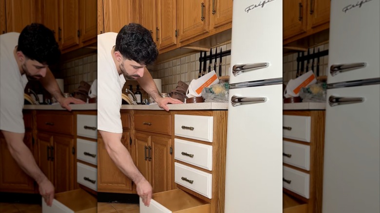 A man adding white vinyl to his wooden kitchen cabinets while next to a white vintage fridge