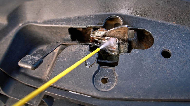 Spray emerging from a straw to lubricate a rusty hood lock