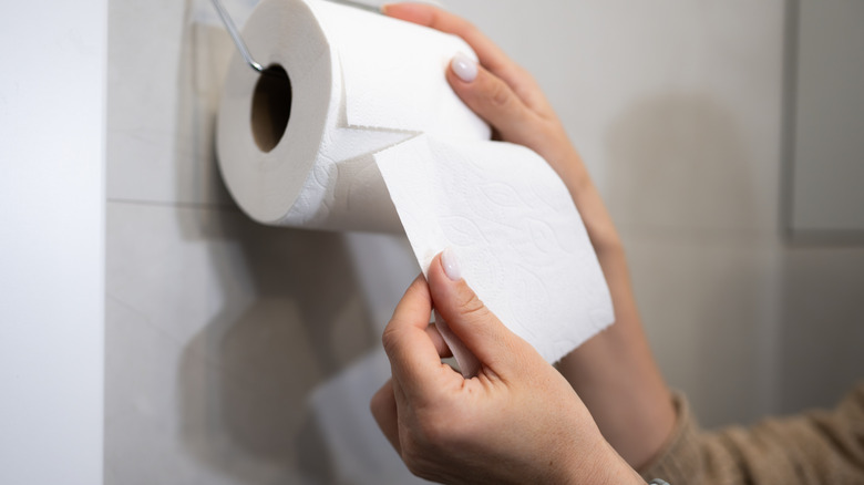 A person tears a piece of toilet paper from a roll that is hanging over
