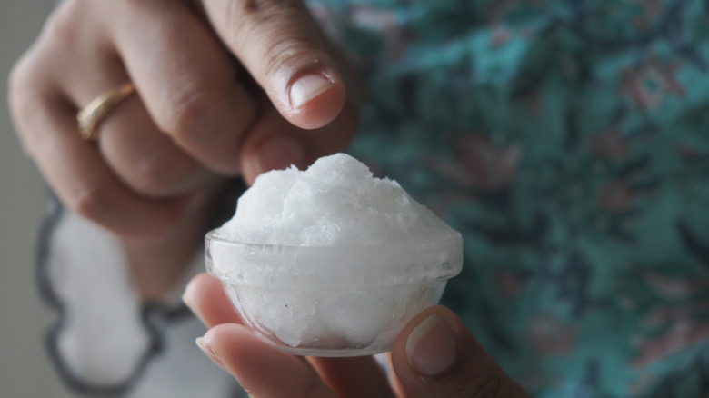A person holding a small bowl of coconut oil