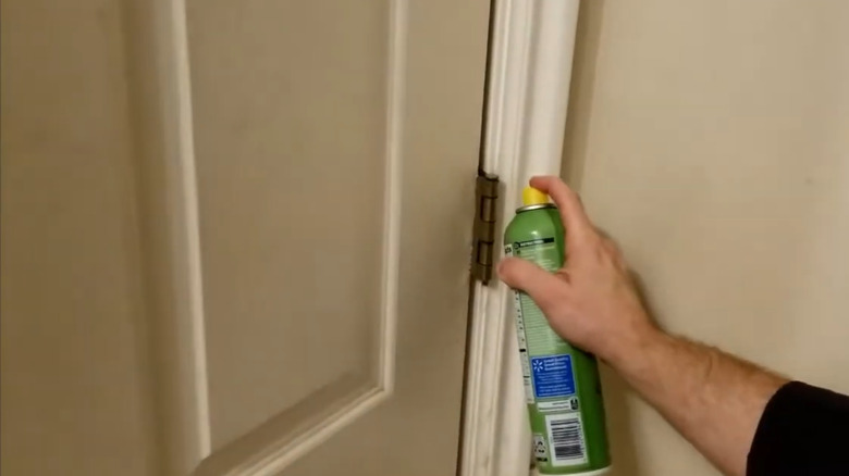 A man spraying a door hinge with cooking spray
