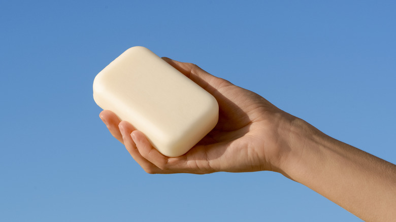 A person holding a bar of soap in front of a blue background