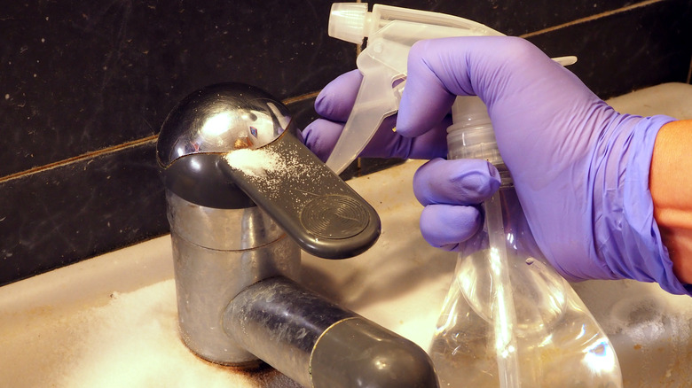 A person using a spray bottle of white vinegar on a rusty faucet