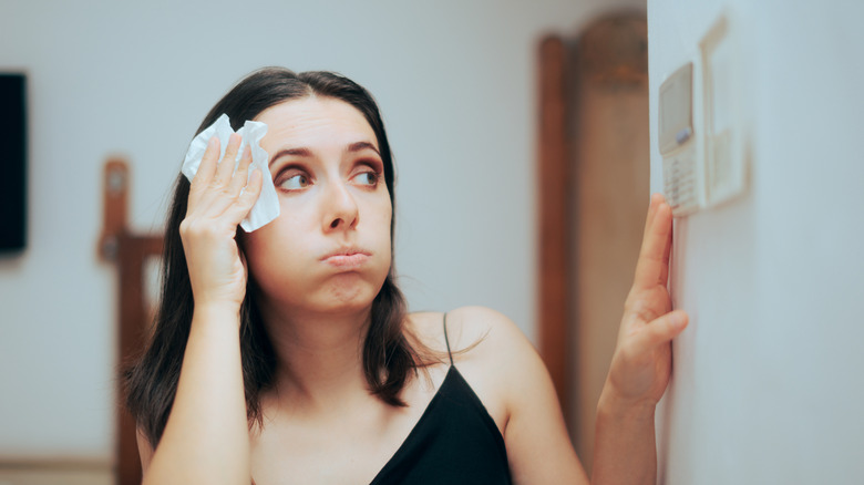 A woman mops sweat off her brow while adjusting a thermostat