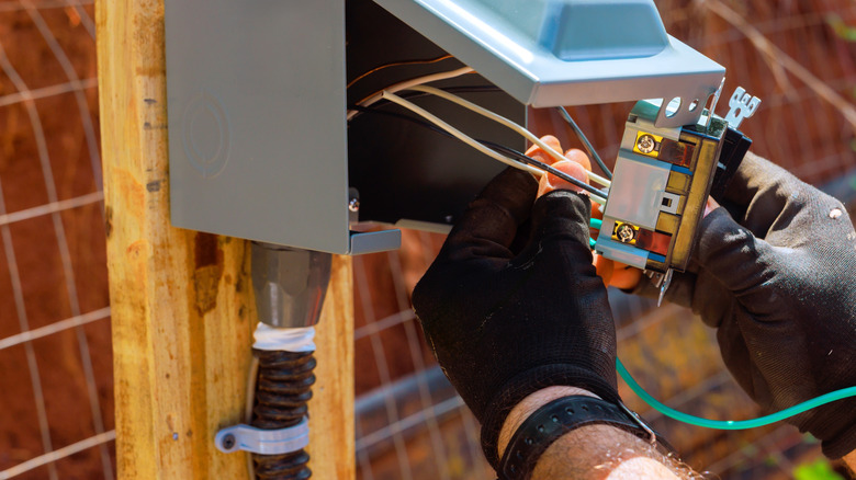 A person's gloved hands working on an outdoor outlet with several different colored wires.