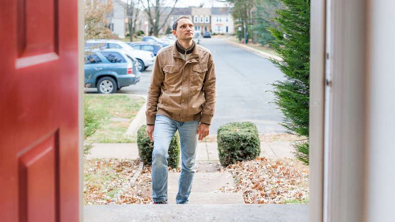 A man walking up to a house's front porch
