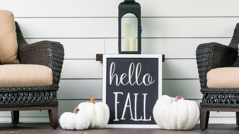 White pumpkins on a porch with two chairs on either side and a chalkboard in the middle