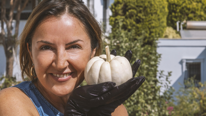 A smiling woman holding a white pumpkin