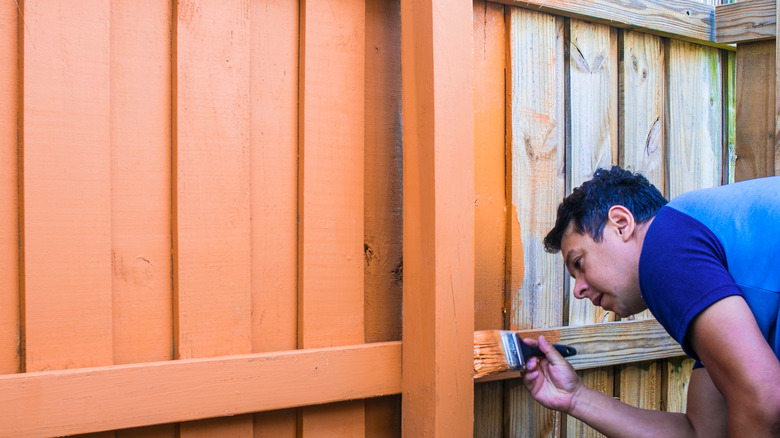 Man painting a fence orange