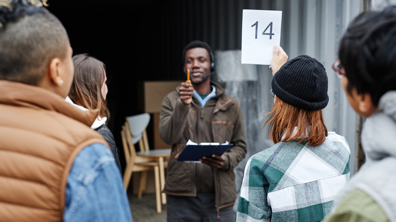 Back view of young woman holding number card bidding on container at outdoor auction