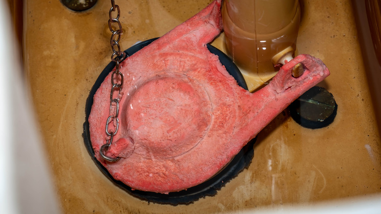 An old flapper valve in a toilet tank with a thin layer of water around it