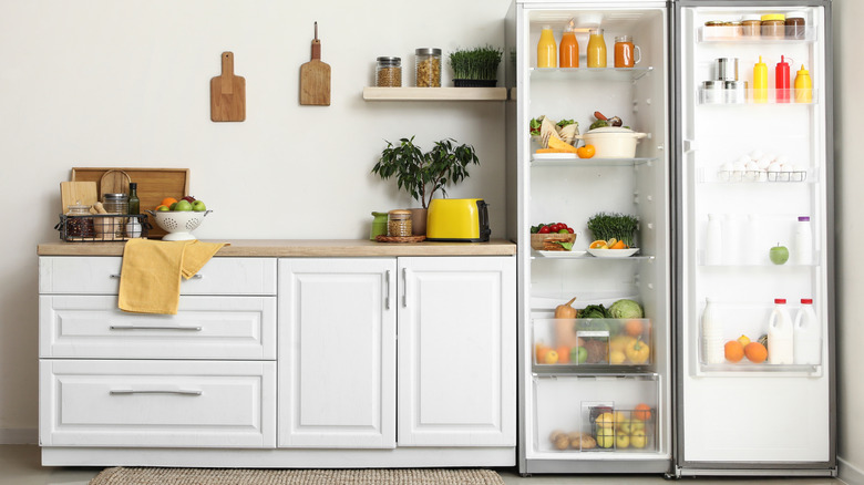 A minimal kitchen with an open refrigerator, showing fruits and vegetables inside.
