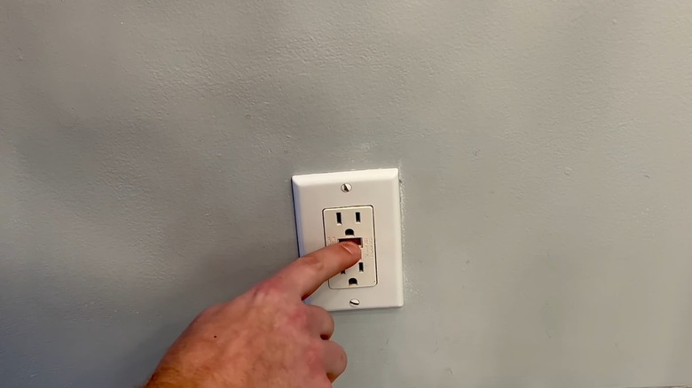 A hand is pressing the "Reset" button on a GFCI outlet