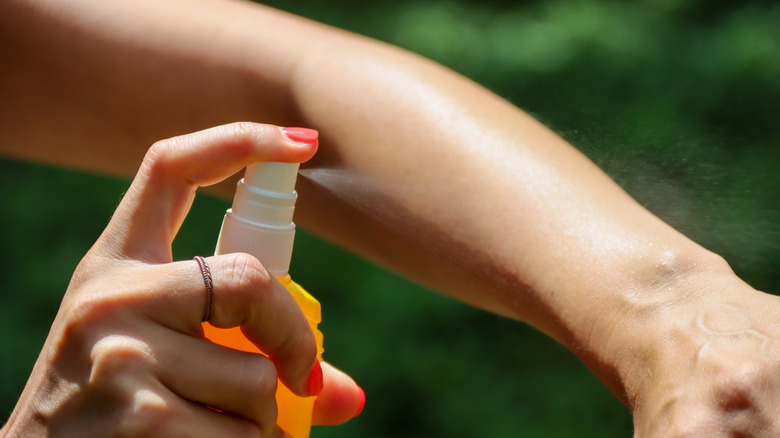 A person sprays mosquito repellent on their arm.