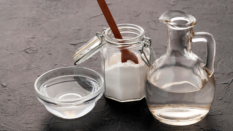 Clear glassware, two filled with clear liquids and one with baking soda, against a gray surface.